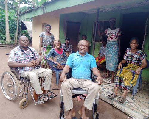 Two men in wheelchairs, provided through the Dubel Disability Foundation, with community members outside a home.